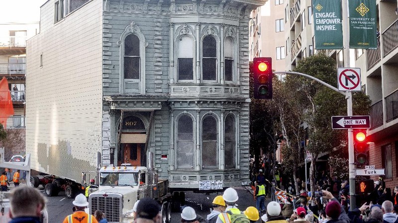 CORRECTS APPROXIMATE COST TO $400,000, INTEAD OF $200,000 - Crowds watch as a truck pulls a Victorian home through San Francisco on Sunday, Feb. 21, 2021. The house, built in 1882, was moved to a new location about six blocks away to make room for a condominium development. According to the consultant overseeing the project, the move cost approximately $400,000 and involved removing street lights, parking meters, and utility lines. (AP Photo/Noah Berger)