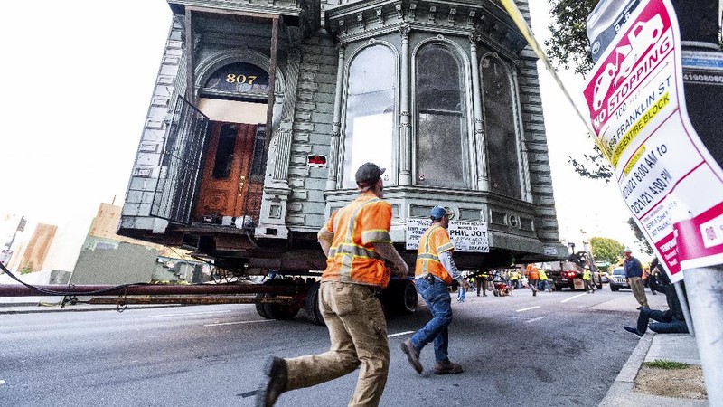 CORRECTS APPROXIMATE COST TO $400,000, INTEAD OF $200,000 - Crowds watch as a truck pulls a Victorian home through San Francisco on Sunday, Feb. 21, 2021. The house, built in 1882, was moved to a new location about six blocks away to make room for a condominium development. According to the consultant overseeing the project, the move cost approximately $400,000 and involved removing street lights, parking meters, and utility lines. (AP Photo/Noah Berger)