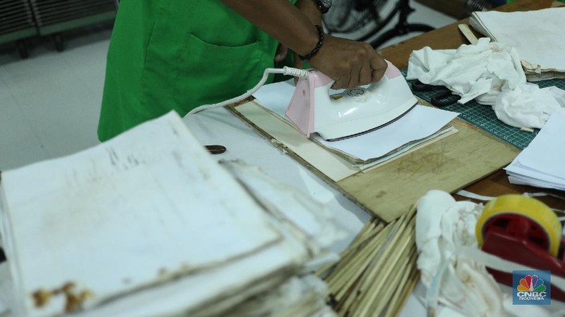 Petugas restorasi ARSIP Nasional Republik Indonesia (ANRI) melakukan perbaikan dokumen milik warga yang terdampak banjir, Jakarta, Senin ( 22/2/2021). Dokumen yang rusak seperti Ijazah hingga akte kelahiran akan diperbaiki 1 sampai 4 Minggu. Contoh arsip keluarga yang bisa diperbaiki dari kerusakan banjir adalah akte, surat perkawinan, akte kelahiran, surat kematian, STTB dll. Maksimal berkas yang diterima 10 lembar.  (CNBC Indonesia/ Tri Susilo)