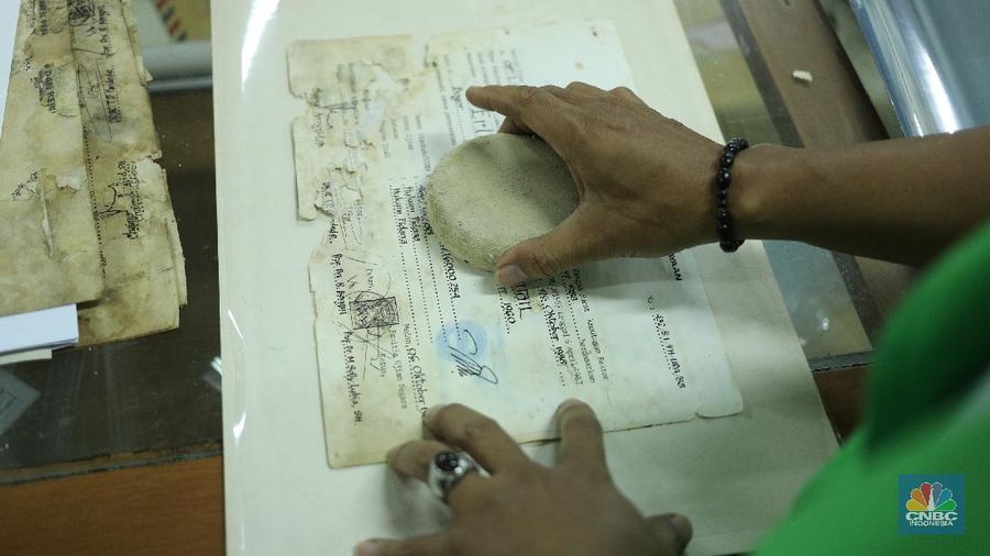 Petugas restorasi ARSIP Nasional Republik Indonesia (ANRI) melakukan perbaikan dokumen milik warga yang terdampak banjir, Jakarta, Senin ( 22/2/2021). Dokumen yang rusak seperti Ijazah hingga akte kelahiran akan diperbaiki 1 sampai 4 Minggu. Contoh arsip keluarga yang bisa diperbaiki dari kerusakan banjir adalah akte, surat perkawinan, akte kelahiran, surat kematian, STTB dll. Maksimal berkas yang diterima 10 lembar.  (CNBC Indonesia/ Tri Susilo)