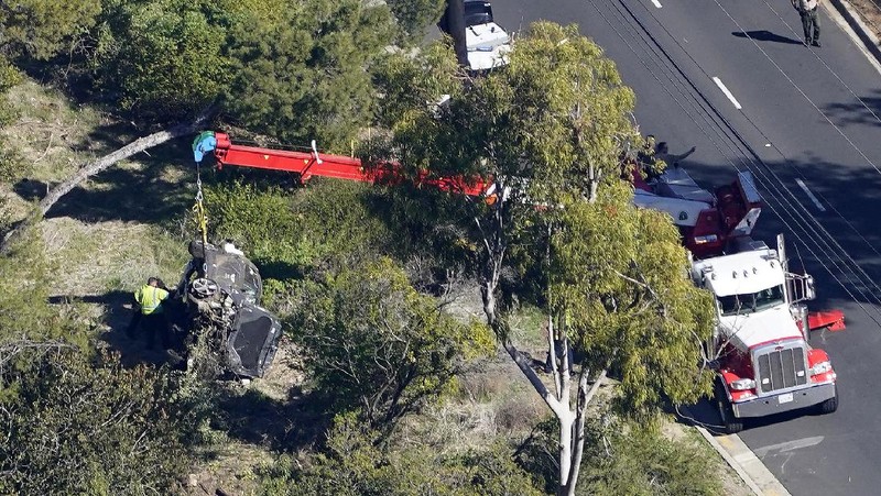 Workers collect debris beside a vehicle after a rollover accident involving golfer Tiger Woods Tuesday, Feb. 23, 2021, in Rancho Palos Verdes, Calif., a suburb of Los Angeles. Woods suffered leg injuries in the one-car accident and was undergoing surgery, authorities and his manager said. (AP Photo/Marcio Jose Sanchez)