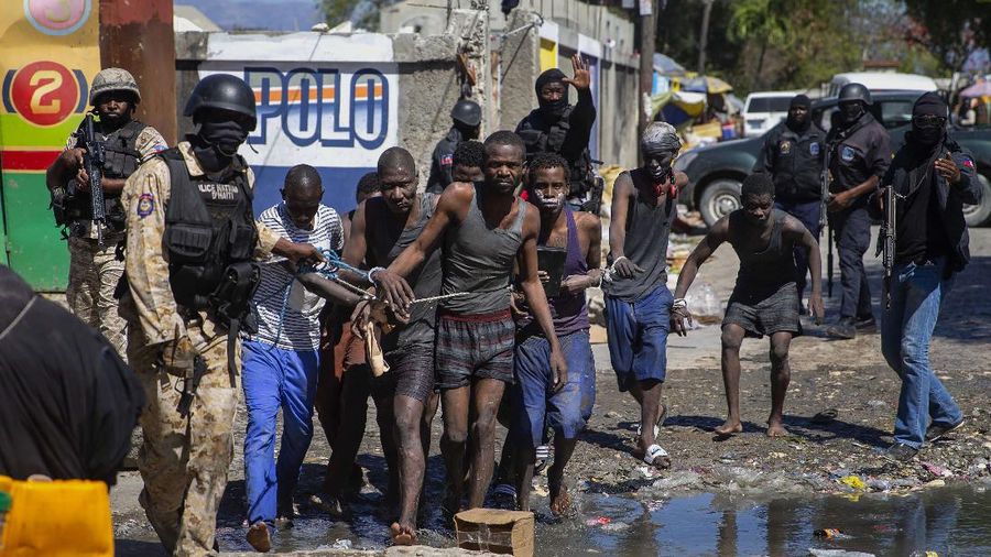 Students rush past the bodies of inmates outside the Croix-des-Bouquets Civil Prison after an attempted breakout in Port-au-Prince, Haiti, Thursday, Feb. 25, 2021. At least seven people were killed and one injured on Thursday after eyewitnesses told The Associated Press that several inmates tried to escape. (AP Photo/Dieu Nalio Chery).
