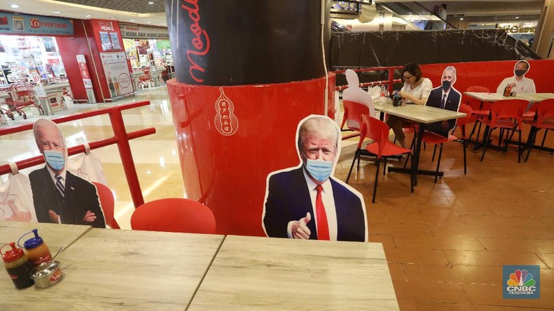 Pengunjung menikmati makanan disamping pembatas jarak bergambar karakter Presiden Amerika Serikat Joe Biden yang menghiasi salah satu pusat restoran cepat saji  di kawasan Kuningan, Jakarta, Selasa (2/3/2021). (CNBC Indonesia/Andrean Kristianto)