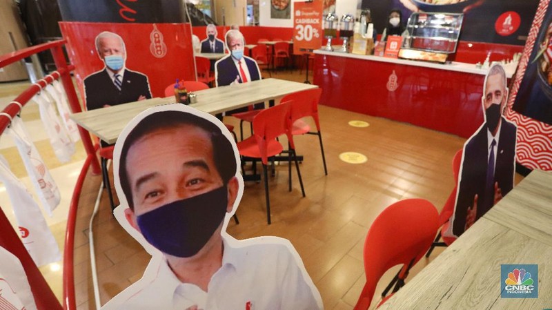 Pengunjung menikmati makanan disamping pembatas jarak bergambar karakter Presiden Amerika Serikat Joe Biden yang menghiasi salah satu pusat restoran cepat saji  di kawasan Kuningan, Jakarta, Selasa (2/3/2021). (CNBC Indonesia/Andrean Kristianto)