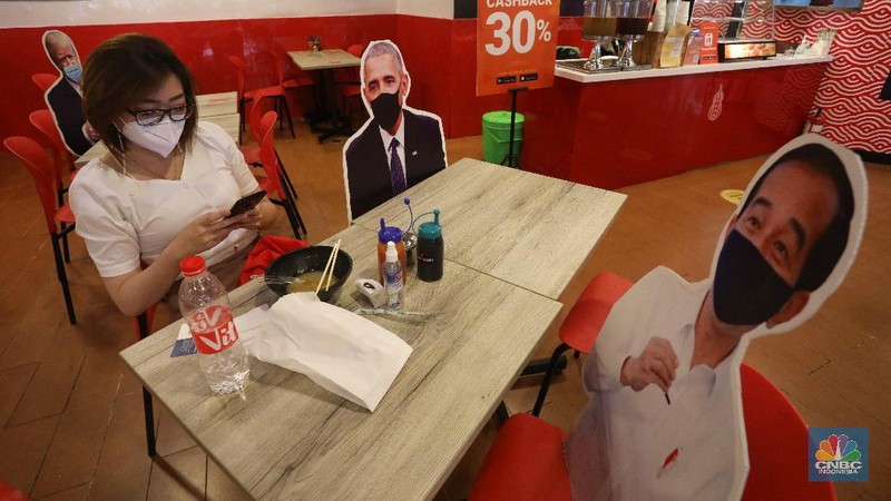 Pengunjung menikmati makanan disamping pembatas jarak bergambar karakter Presiden Amerika Serikat Joe Biden yang menghiasi salah satu pusat restoran cepat saji  di kawasan Kuningan, Jakarta, Selasa (2/3/2021). (CNBC Indonesia/Andrean Kristianto)