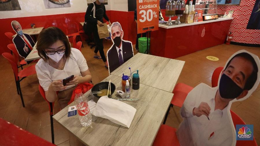 Pengunjung menikmati makanan disamping pembatas jarak bergambar karakter Presiden Amerika Serikat Joe Biden yang menghiasi salah satu pusat restoran cepat saji di kawasan Kuningan, Jakarta, Selasa (2/3/2021). (CNBC Indonesia/Andrean Kristianto)