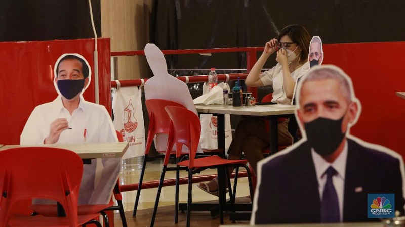 Pengunjung menikmati makanan disamping pembatas jarak bergambar karakter Presiden Amerika Serikat Joe Biden yang menghiasi salah satu pusat restoran cepat saji  di kawasan Kuningan, Jakarta, Selasa (2/3/2021). (CNBC Indonesia/Andrean Kristianto)