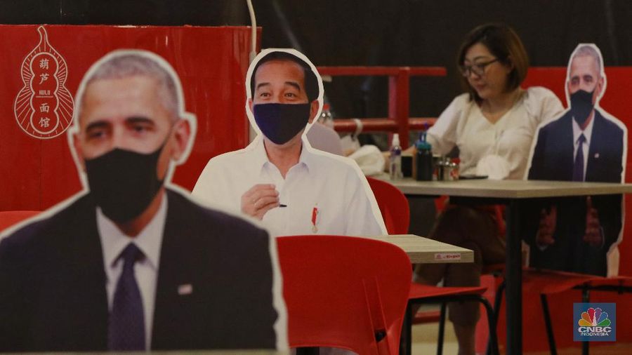 Pengunjung menikmati makanan disamping pembatas jarak bergambar karakter Presiden Amerika Serikat Joe Biden yang menghiasi salah satu pusat restoran cepat saji  di kawasan Kuningan, Jakarta, Selasa (2/3/2021). (CNBC Indonesia/Andrean Kristianto)