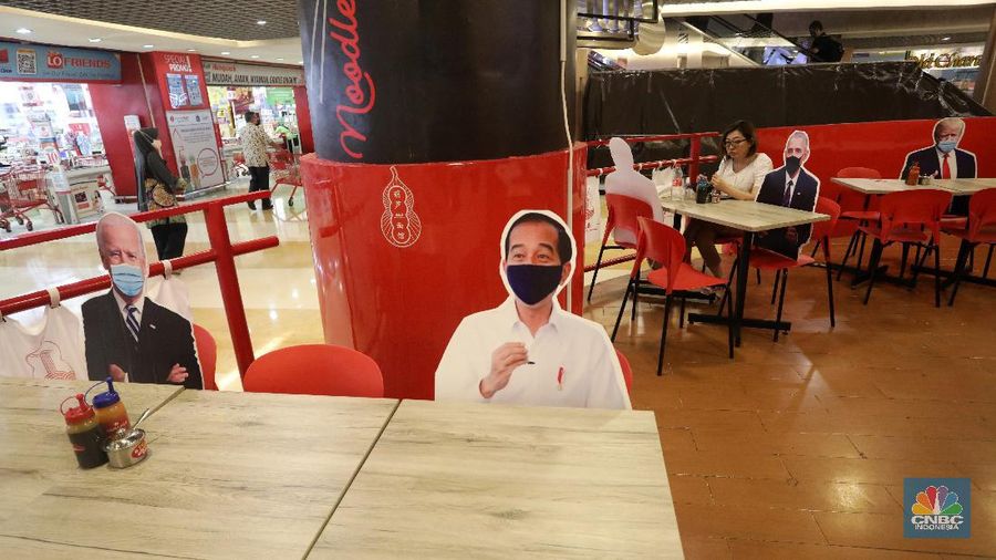 Pengunjung menikmati makanan disamping pembatas jarak bergambar karakter Presiden Amerika Serikat Joe Biden yang menghiasi salah satu pusat restoran cepat saji  di kawasan Kuningan, Jakarta, Selasa (2/3/2021). (CNBC Indonesia/Andrean Kristianto)