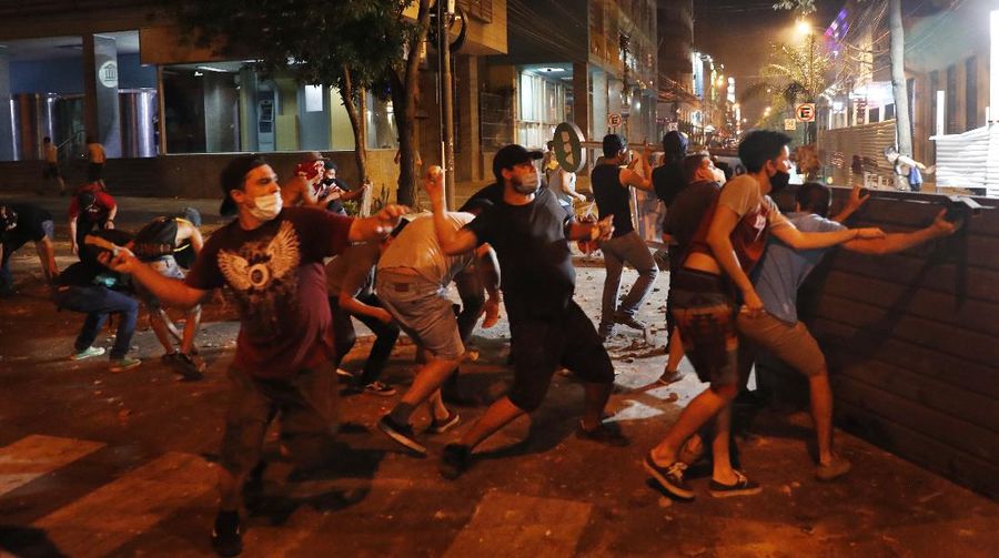 A protester slips in clashes with police during protest against the government of President Mario Abdo Benitez in response to the shortage of medications for COVID-19 patients in hospitals and the low availability of the vaccine against the new coronavirus, amid the resignation of the country's health minister, in Asuncion, Paraguay, Friday, March 5, 2021. (AP Photo/Jorge Saenz)