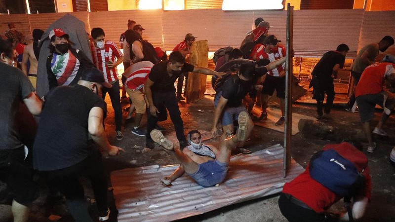 A protester slips in clashes with police during protest against the government of President Mario Abdo Benitez in response to the shortage of medications for COVID-19 patients in hospitals and the low availability of the vaccine against the new coronavirus, amid the resignation of the country's health minister, in Asuncion, Paraguay, Friday, March 5, 2021. (AP Photo/Jorge Saenz)