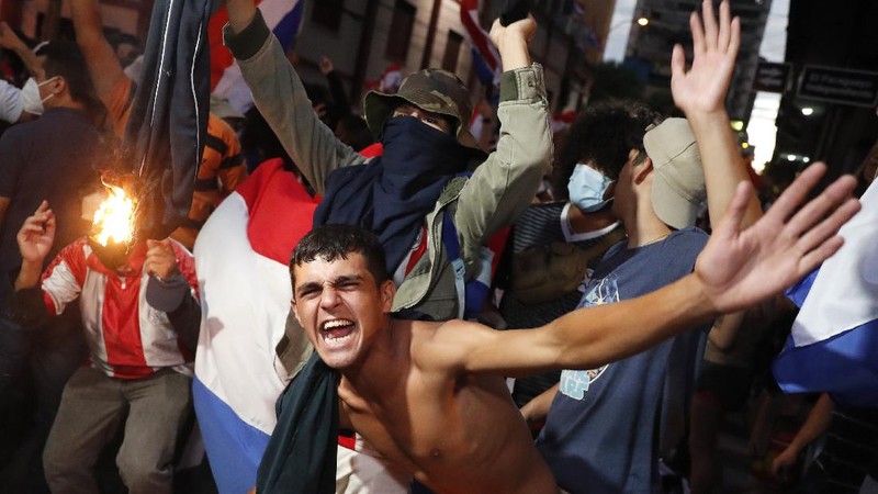 A protester slips in clashes with police during protest against the government of President Mario Abdo Benitez in response to the shortage of medications for COVID-19 patients in hospitals and the low availability of the vaccine against the new coronavirus, amid the resignation of the country's health minister, in Asuncion, Paraguay, Friday, March 5, 2021. (AP Photo/Jorge Saenz)