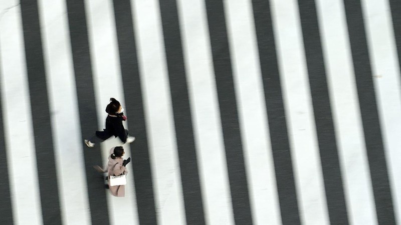 People wearing protective masks to help curb the spread of the coronavirus run along a pedestrian crossing Thursday, Feb. 25, 2021, in Tokyo. The Japanese capital confirmed more than 340 new coronavirus cases on Thursday. (AP Photo/Eugene Hoshiko)