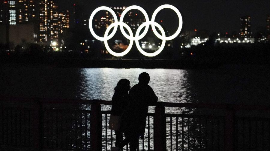 A man and a woman stand with the backdrop of the Olympic rings floating in the water in the Odaiba section in Tokyo, Wednesday, March 3, 2021. (AP Photo/Eugene Hoshiko)