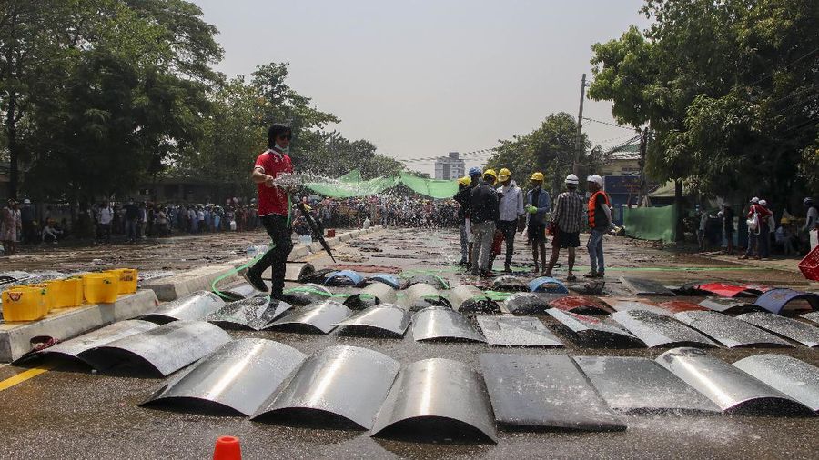 An anti-coup protester sprays water on metal-makeshift shields to prevent from heat in hot-sunny weather in Yangon, Myanmar Tuesday, March 9, 2021. Demonstrators in Myanmar's biggest city came out Monday night for their first mass protests in defiance of an 8 p.m. curfew, seeking to show support for an estimated 200 students trapped by security forces in a small area of one neighborhood. (AP Photo)