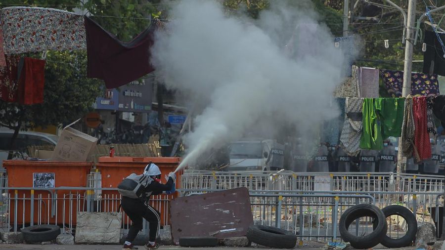 An anti-coup protester uses a fire extinguisher behind a line of women's clothing hanged across a road to deter security personnel from entering the protest area in Yangon, Myanmar Tuesday, March 9, 2021. In Burmese culture, walking underneath women's clothing is believed to weaken the power of men and bring bad fortune. (AP Photo)