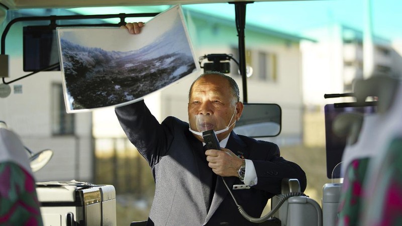 Fumio Ito, head of public relations at Minami Sanriku Hotel Kanyo, tells his experience of 2011 tsunami disaster in the area to participants inside a bus during the 