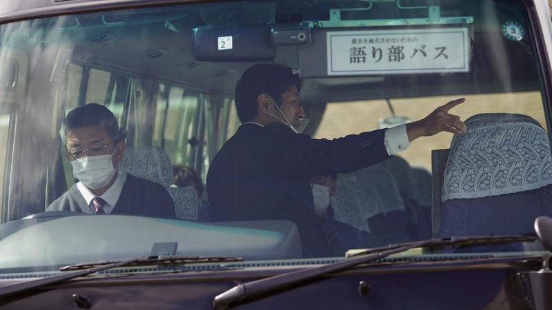 Fumio Ito, head of public relations at Minami Sanriku Hotel Kanyo, tells his experience of 2011 tsunami disaster in the area to participants inside a bus during the 