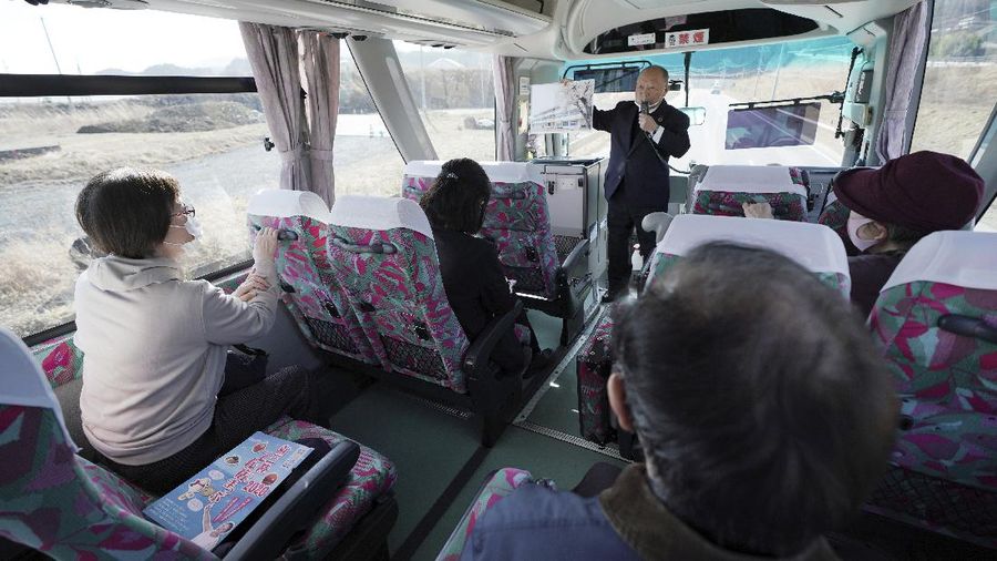 Fumio Ito, head of public relations at Minami Sanriku Hotel Kanyo, tells his experience of 2011 tsunami disaster in the area to participants inside a bus during the 
