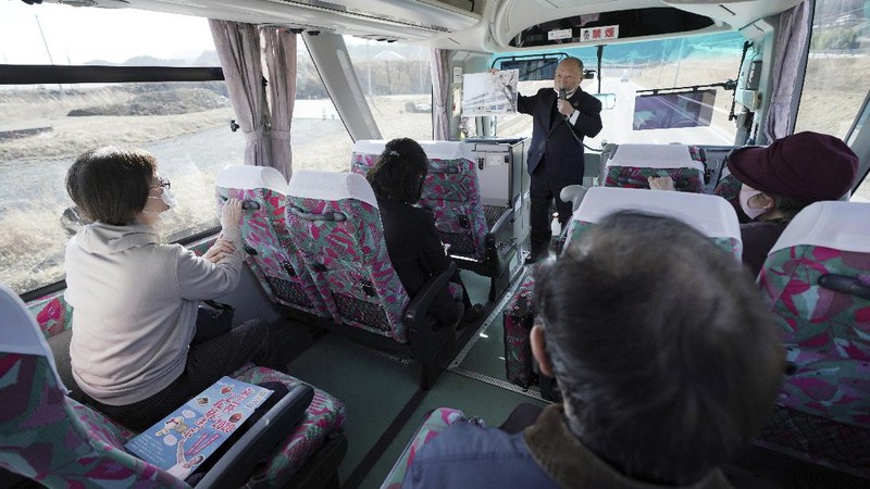 Fumio Ito, head of public relations at Minami Sanriku Hotel Kanyo, tells his experience of 2011 tsunami disaster in the area to participants inside a bus during the 