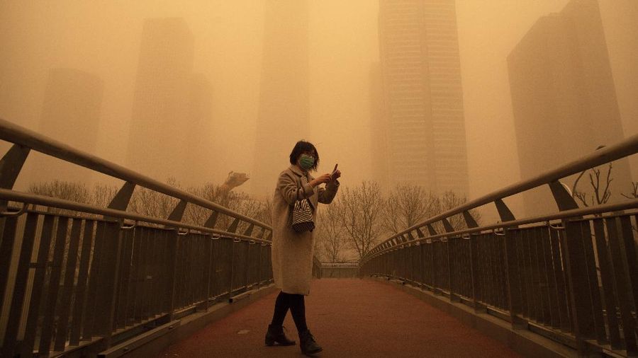 People wait to cross an intersection amid a sandstorm during the morning rush hour in Beijing, Monday, March 15, 2021. The sandstorm brought a tinted haze to Beijing's skies and sent air quality indices soaring on Monday. (AP Photo/Mark Schiefelbein)