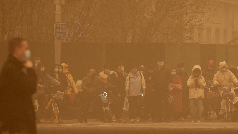 People wait to cross an intersection amid a sandstorm during the morning rush hour in Beijing, Monday, March 15, 2021. The sandstorm brought a tinted haze to Beijing's skies and sent air quality indices soaring on Monday. (AP Photo/Mark Schiefelbein)