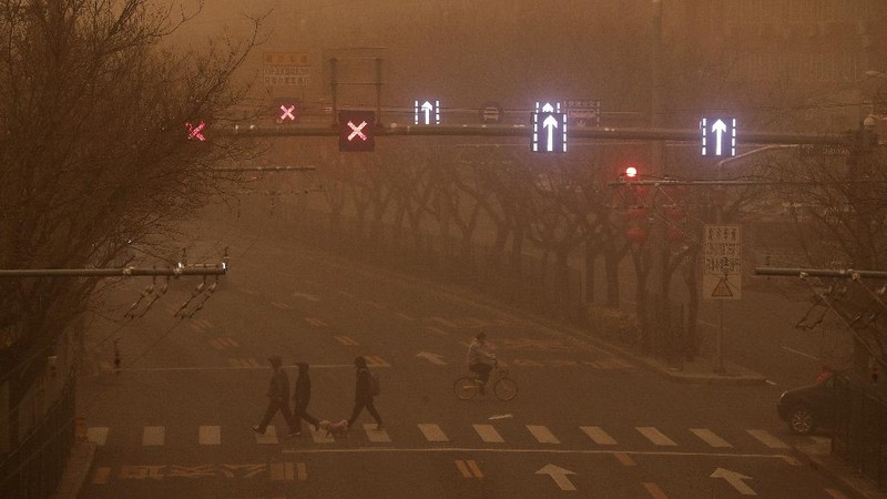 People wait to cross an intersection amid a sandstorm during the morning rush hour in Beijing, Monday, March 15, 2021. The sandstorm brought a tinted haze to Beijing's skies and sent air quality indices soaring on Monday. (AP Photo/Mark Schiefelbein)