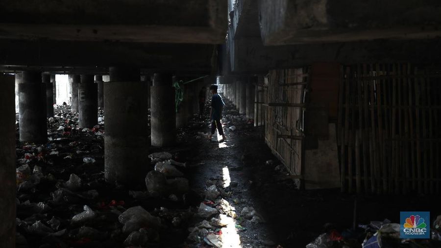 Warga melintas di kolong tol  Ir Wiyoto, Kelurahan Papanggo, Tanjung Priok, Jakarta, Kamis (18/3/2021). Tumpukan sampah plastik makanan dan limbah rumah tangga Tampak sudah melebur dengan tanah. Pantauan CNBC Indonesia di lokasi warga masih ada yang membuang sampah dilokasi walaupun sudah di tegur dengan warga sekitar. Yanto salah satu warga mengatakan 