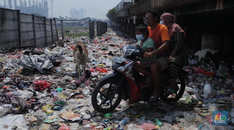 Warga melintas di kolong tol  Ir Wiyoto, Kelurahan Papanggo, Tanjung Priok, Jakarta, Kamis (18/3/2021). Tumpukan sampah plastik makanan dan limbah rumah tangga Tampak sudah melebur dengan tanah. Pantauan CNBC Indonesia di lokasi warga masih ada yang membuang sampah dilokasi walaupun sudah di tegur dengan warga sekitar. Yanto salah satu warga mengatakan 