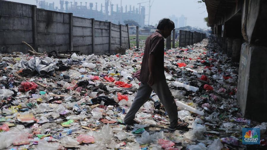 Warga melintas di kolong tol Ir Wiyoto, Kelurahan Papanggo, Tanjung Priok, Jakarta, Kamis (18/3/2021). Tumpukan sampah plastik makanan dan limbah rumah tangga Tampak sudah melebur dengan tanah. Pantauan CNBC Indonesia di lokasi warga masih ada yang membuang sampah dilokasi walaupun sudah di tegur dengan warga sekitar. Yanto salah satu warga mengatakan