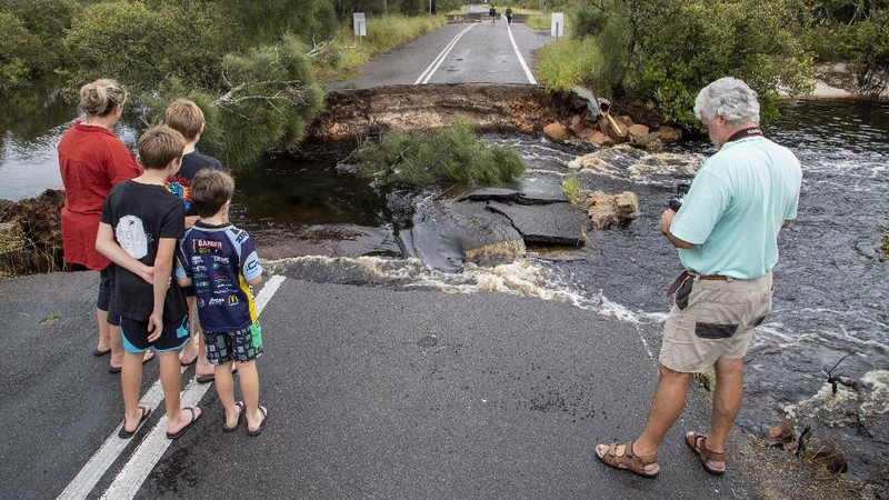 People stand at a washed out section of road at Port Stephens 200 kilometers (124 miles) north of Sydney, Australia, Saturday, March 20, 2021. People across New South Wales have been warned to expect intense rain and potentially life-threatening flooding, with Sydney predicted to be deluged with up to 200 millimeters of rain in one day. (AP Photo/Mark Baker)