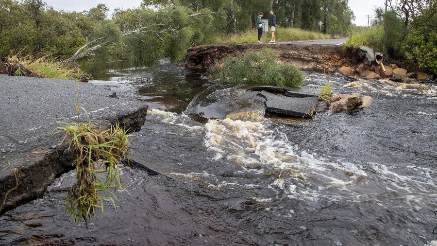 People stand at a washed out section of road at Port Stephens 200 kilometers (124 miles) north of Sydney, Australia, Saturday, March 20, 2021. People across New South Wales have been warned to expect intense rain and potentially life-threatening flooding, with Sydney predicted to be deluged with up to 200 millimeters of rain in one day. (AP Photo/Mark Baker)