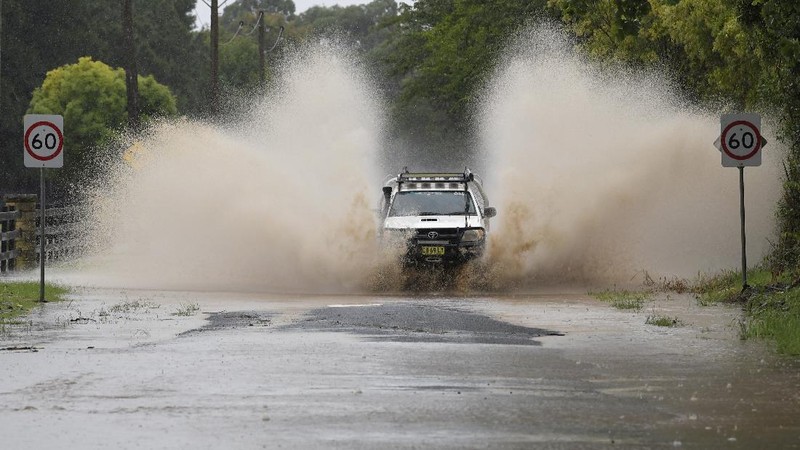 People stand at a washed out section of road at Port Stephens 200 kilometers (124 miles) north of Sydney, Australia, Saturday, March 20, 2021. People across New South Wales have been warned to expect intense rain and potentially life-threatening flooding, with Sydney predicted to be deluged with up to 200 millimeters of rain in one day. (AP Photo/Mark Baker)