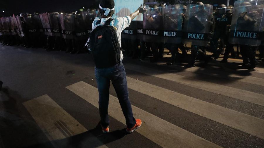A riot policeman advances towards a man kneeling on the road after the dispersal of protesters who removed container vans used as a barricade in front of the Grand Palace Saturday, March 20, 2021 in Bangkok, Thailand. Thailand's student-led pro-democracy movement is holding a rally in the Thai capital, seeking to press demands that include freedom for their leaders, who are being held without bail on charges of defaming the monarchy. (AP Photo/Sakchai Lalit)