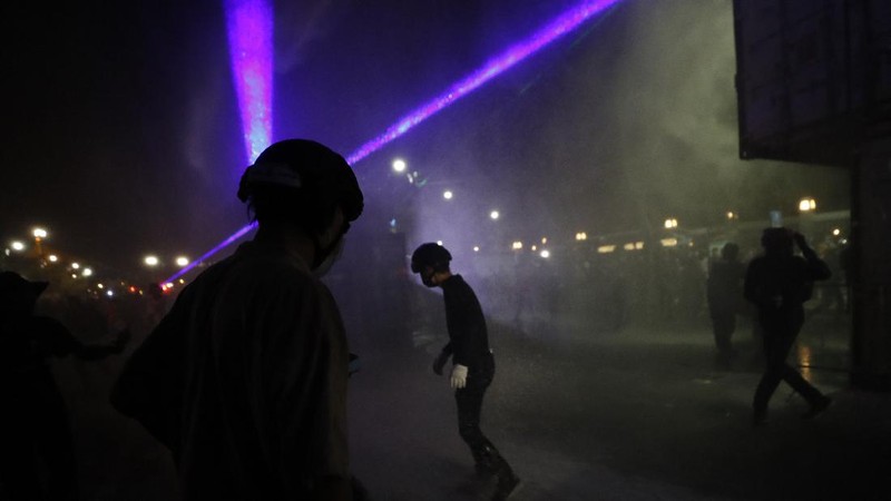 A riot policeman advances towards a man kneeling on the road after the dispersal of protesters who removed container vans used as a barricade in front of the Grand Palace Saturday, March 20, 2021 in Bangkok, Thailand. Thailand's student-led pro-democracy movement is holding a rally in the Thai capital, seeking to press demands that include freedom for their leaders, who are being held without bail on charges of defaming the monarchy. (AP Photo/Sakchai Lalit)