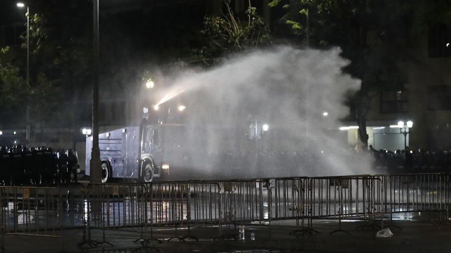 A riot policeman advances towards a man kneeling on the road after the dispersal of protesters who removed container vans used as a barricade in front of the Grand Palace Saturday, March 20, 2021 in Bangkok, Thailand. Thailand's student-led pro-democracy movement is holding a rally in the Thai capital, seeking to press demands that include freedom for their leaders, who are being held without bail on charges of defaming the monarchy. (AP Photo/Sakchai Lalit)