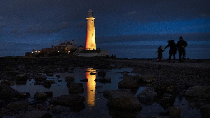 St Mary's Lighthouse is illuminated yellow during the National Day of Reflection, on the anniversary of the first national lockdown to prevent the spread of coronavirus, in Whitley Bay, England, Tuesday March 23, 2021.  Britain is marking the anniversary of being in lockdown for one year because of the pandemic, by illuminating public buildings in yellow light.(Owen Humphreys/PA via AP)