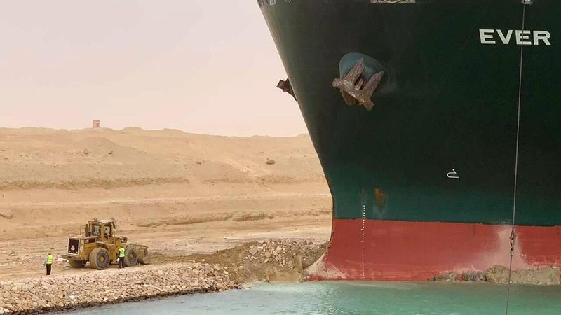 In this photo released by the Suez Canal Authority, a boat navigates in front of a massive cargo ship, named the Ever Green, rear, sits grounded Wednesday, March 24, 2021, after it turned sideways in Egypt’s Suez Canal, blocking traffic in a crucial East-West waterway for global shipping. An Egyptian official warned Wednesday it could take at least two days to clear the ship. (Suez Canal Authority via AP)