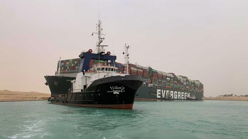 In this photo released by the Suez Canal Authority, a boat navigates in front of a massive cargo ship, named the Ever Green, rear, sits grounded Wednesday, March 24, 2021, after it turned sideways in Egypt’s Suez Canal, blocking traffic in a crucial East-West waterway for global shipping. An Egyptian official warned Wednesday it could take at least two days to clear the ship. (Suez Canal Authority via AP)