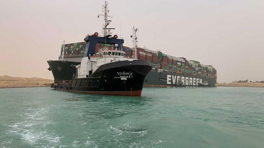In this photo released by the Suez Canal Authority, a boat navigates in front of a massive cargo ship, named the Ever Green, rear, sits grounded Wednesday, March 24, 2021, after it turned sideways in Egypt’s Suez Canal, blocking traffic in a crucial East-West waterway for global shipping. An Egyptian official warned Wednesday it could take at least two days to clear the ship. (Suez Canal Authority via AP)