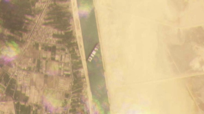 In this photo released by the Suez Canal Authority, a boat navigates in front of a massive cargo ship, named the Ever Green, rear, sits grounded Wednesday, March 24, 2021, after it turned sideways in Egypt’s Suez Canal, blocking traffic in a crucial East-West waterway for global shipping. An Egyptian official warned Wednesday it could take at least two days to clear the ship. (Suez Canal Authority via AP)