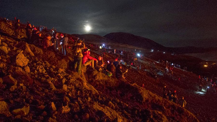 People watch as lava flows from an eruption of a volcano on the Reykjanes Peninsula in southwestern Iceland late on Monday, March 29, 2021. Iceland's latest volcano eruption is still attracting crowds of people hoping to get close to the gentle lava flows. The eruption in Geldingadalur, near Iceland's capital Reykjavik, is not seen as a threat to nearby towns and the slow flows mean people can get close to action without too much harm. (AP Photo/Marco Di Marco)