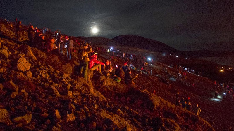 People watch as lava flows from an eruption of a volcano on the Reykjanes Peninsula in southwestern Iceland late on Monday, March 29, 2021. Iceland's latest volcano eruption is still attracting crowds of people hoping to get close to the gentle lava flows. The eruption in Geldingadalur, near Iceland's capital Reykjavik, is not seen as a threat to nearby towns and the slow flows mean people can get close to action without too much harm. (AP Photo/Marco Di Marco)
