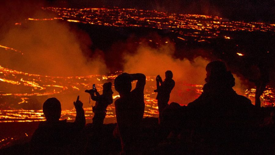 People watch as lava flows from an eruption of a volcano on the Reykjanes Peninsula in southwestern Iceland late on Monday, March 29, 2021. Iceland's latest volcano eruption is still attracting crowds of people hoping to get close to the gentle lava flows. The eruption in Geldingadalur, near Iceland's capital Reykjavik, is not seen as a threat to nearby towns and the slow flows mean people can get close to action without too much harm. (AP Photo/Marco Di Marco)