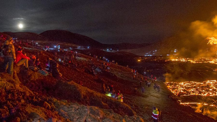 People watch as lava flows from an eruption of a volcano on the Reykjanes Peninsula in southwestern Iceland late on Monday, March 29, 2021. Iceland's latest volcano eruption is still attracting crowds of people hoping to get close to the gentle lava flows. The eruption in Geldingadalur, near Iceland's capital Reykjavik, is not seen as a threat to nearby towns and the slow flows mean people can get close to action without too much harm. (AP Photo/Marco Di Marco)