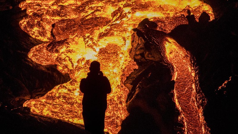People watch as lava flows from an eruption of a volcano on the Reykjanes Peninsula in southwestern Iceland late on Monday, March 29, 2021. Iceland's latest volcano eruption is still attracting crowds of people hoping to get close to the gentle lava flows. The eruption in Geldingadalur, near Iceland's capital Reykjavik, is not seen as a threat to nearby towns and the slow flows mean people can get close to action without too much harm. (AP Photo/Marco Di Marco)