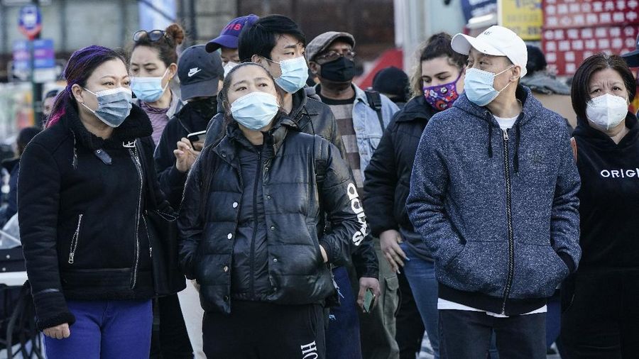 Pedestrians wait to cross the street in the Flushing neighborhood of the Queens borough of New York, Tuesday, March 30, 2021.  Authorities are searching for a man who viciously attacked an Asian American woman near New York City’s Times Square are asking the public for help — not only in locating the suspect but also in doing its part to disrupt further assaults. (AP Photo/Frank Franklin II)