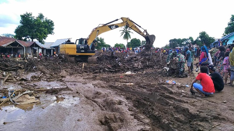 People watch as an excavator clears debris at a flood-affected area in Waiwerang, on Adonara Island, East Nusa Tenggara province, Indonesia, Tuesday, April 6, 2021. Rescuers in remote eastern Indonesia were digging through the debris of a landslide Tuesday in search of people believed to be buried in one of several disasters brought on by severe weather in the Southeast Asian nation and neighboring East Timor. (AP Photo/Rofinus Monteiro)
