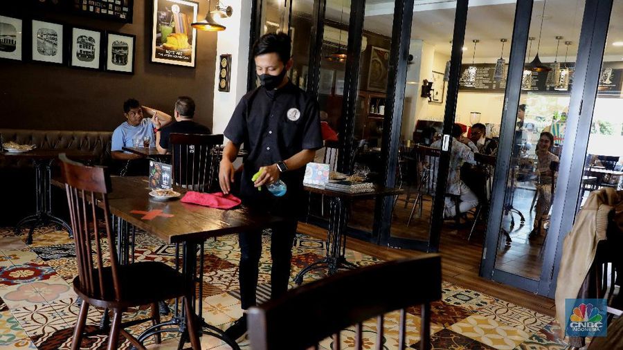Petugas membersihkan meja makanan di Restoran di Kawasan Benhil, Jakarta, Selasa 6/4. Perhimpunan Hotel dan Restoran Indonesia (PHRI) Jakarta ingin pemerintah meningkatkan kapasitas jumlah pengunjung yang bisa makan di tempat alias dine in di tempat makan menjadi 75 persen saat masa buka bersama (bukber) puasa sepanjang Ramadan. Saat ini, kapasitas pengunjung dine in hanya boleh 50 persen. Kebijakan ini diterapkan karena pemerintah masih melangsungkan Pemberlakuan Pembatasan Kegiatan Masyarakat (PPKM) Mikro. Terkait hal ini, Pelaksana Tugas (Plt) Kepala Dinas Pariwisata dan Ekonomi Kreatif DKI Jakarta Gumilar Ekalaya mengatakan belum ada perubahan aturan terkait kapasitas jam operasional restoran saat momen buka puasa bersama seperti dikutip CNN Indonesia. Namun, pemerintah tetap membuka masukan dari pengusaha. Pelaksana tugas (Plt) Kepala Dinas Pariwisata dan Ekonomi Kreatif DKI Jakarta, Gumilar Ekalaya juga mengatakan pihaknya tidak melarang pelaksanaan kegiatan buka puasa bersama (bukber) di restoran atau rumah makan di masa pandemi Covid-19. Menurut Gumilar, waktu pelaksanaan kegiatan bukber tidak melanggar ketentuan dalam PPKM Mikro. Meski tidak melarang, Gumilar mengingatkan kegiatan buka bersama harus tetap menerapkan protokol kesehatan. (CNBC Indonesia/Muhammad Sabki)