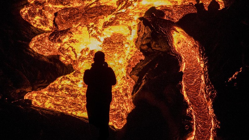People watch as lava flows from an eruption of a volcano on the Reykjanes Peninsula in southwestern Iceland late on Monday, March 29, 2021. Iceland's latest volcano eruption is still attracting crowds of people hoping to get close to the gentle lava flows. (AP Photo/Marco Di Marco)